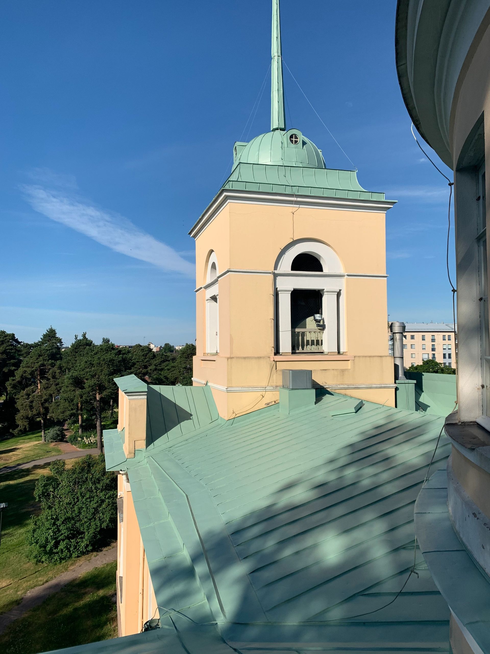 Beige torni vihreällä katolla ja huipulla suuremman rakennuksen vieressä kirkkaan sinisen taivaan alla