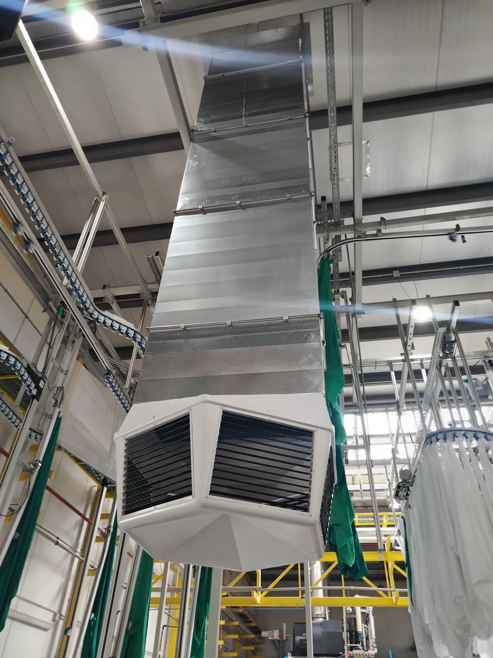 Gran sistema de ventilación industrial suspendido del techo. Conductos metálicos con manguera verde.