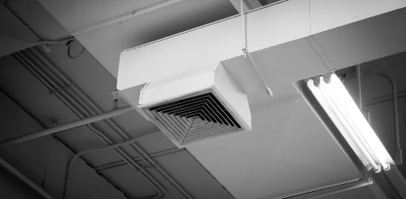 Imagen en blanco y negro de un techo con ventilación de aire y lámparas fluorescentes.