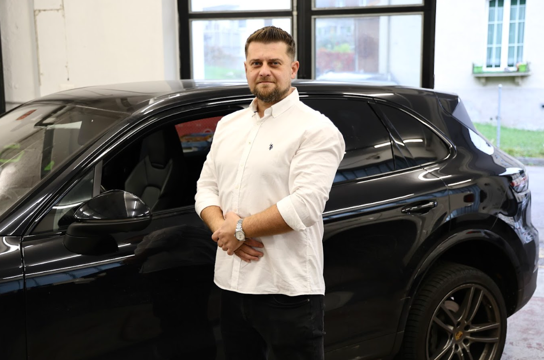 Die Hand einer Person wischt einen Automotor im Motorraum mit einem braunen Tuch ab.