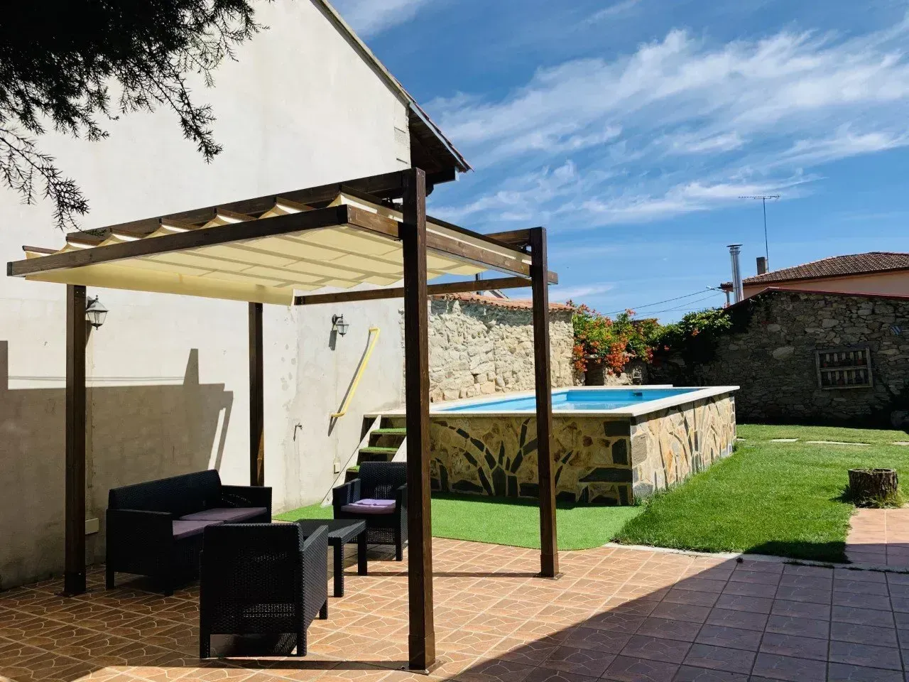 Un patio con pérgola y una piscina al fondo.