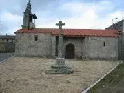 Una pequeña iglesia de piedra con techo de tejas rojas y una cruz delante de ella.