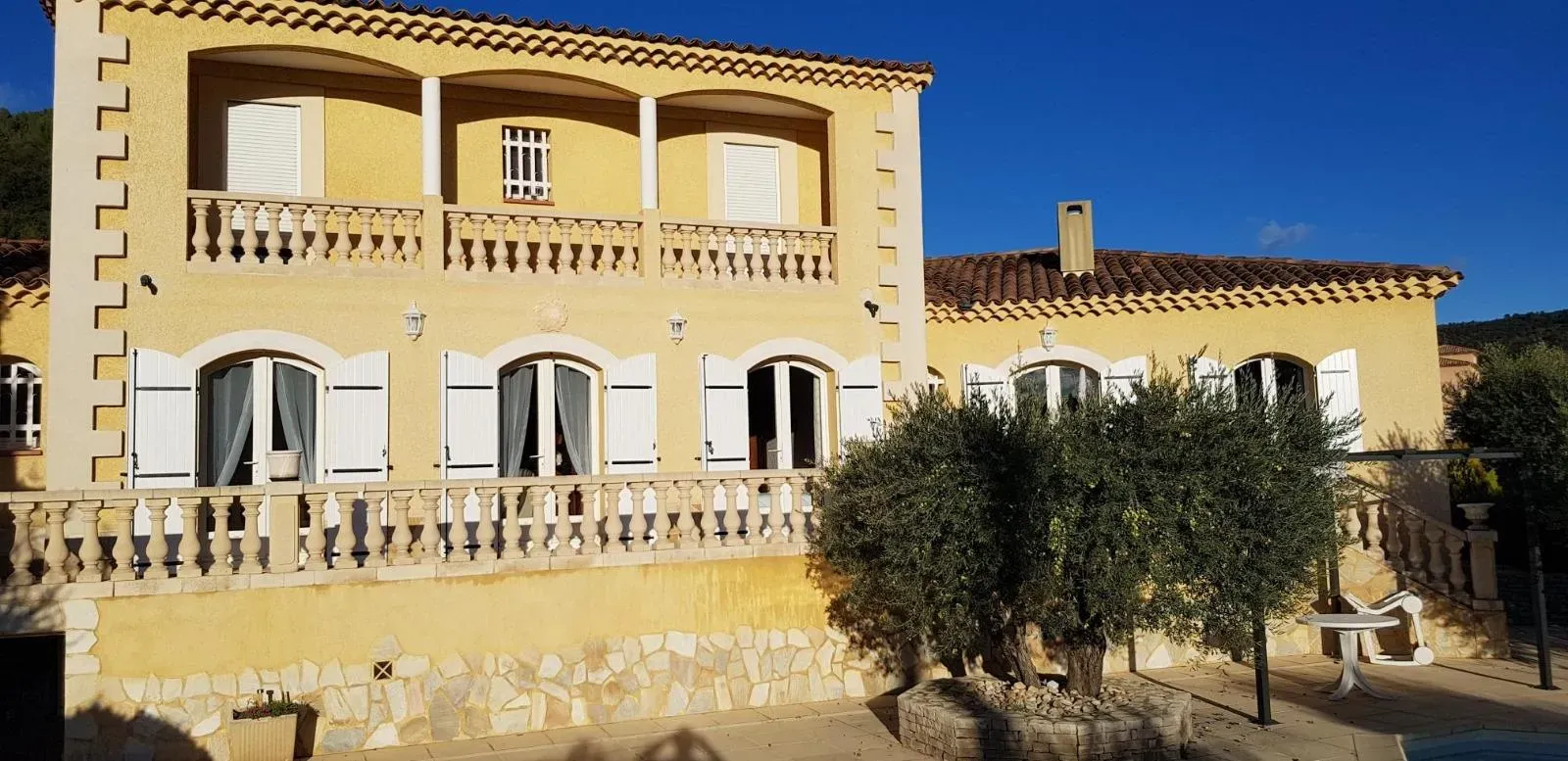 Bâtiment en stuc jaune avec volets blancs et toit de tuiles se détachant sur un ciel bleu limpide.