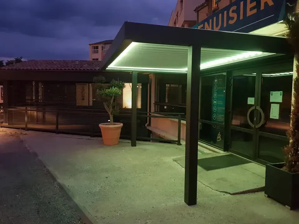 Extérieur de l'entrée d'un bâtiment avec auvent, éclairée par des lumières vertes