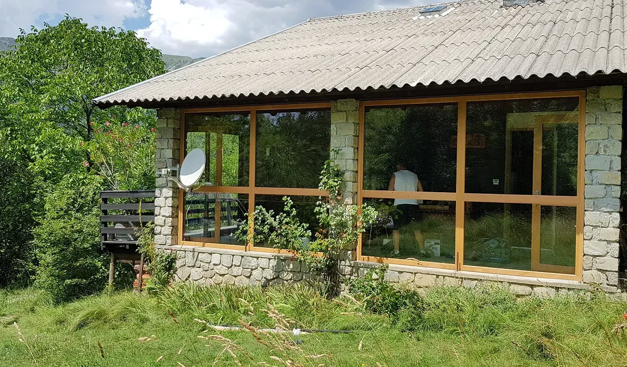 Une petite maison en pierre avec de grandes fenêtres, une antenne parabolique et un jardin verdoyant