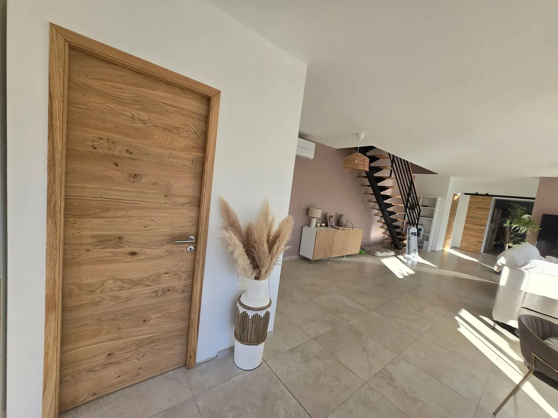 Porte en bois dans une maison moderne, avec un vase d'herbes de la pampa et un escalier en arrière-plan.