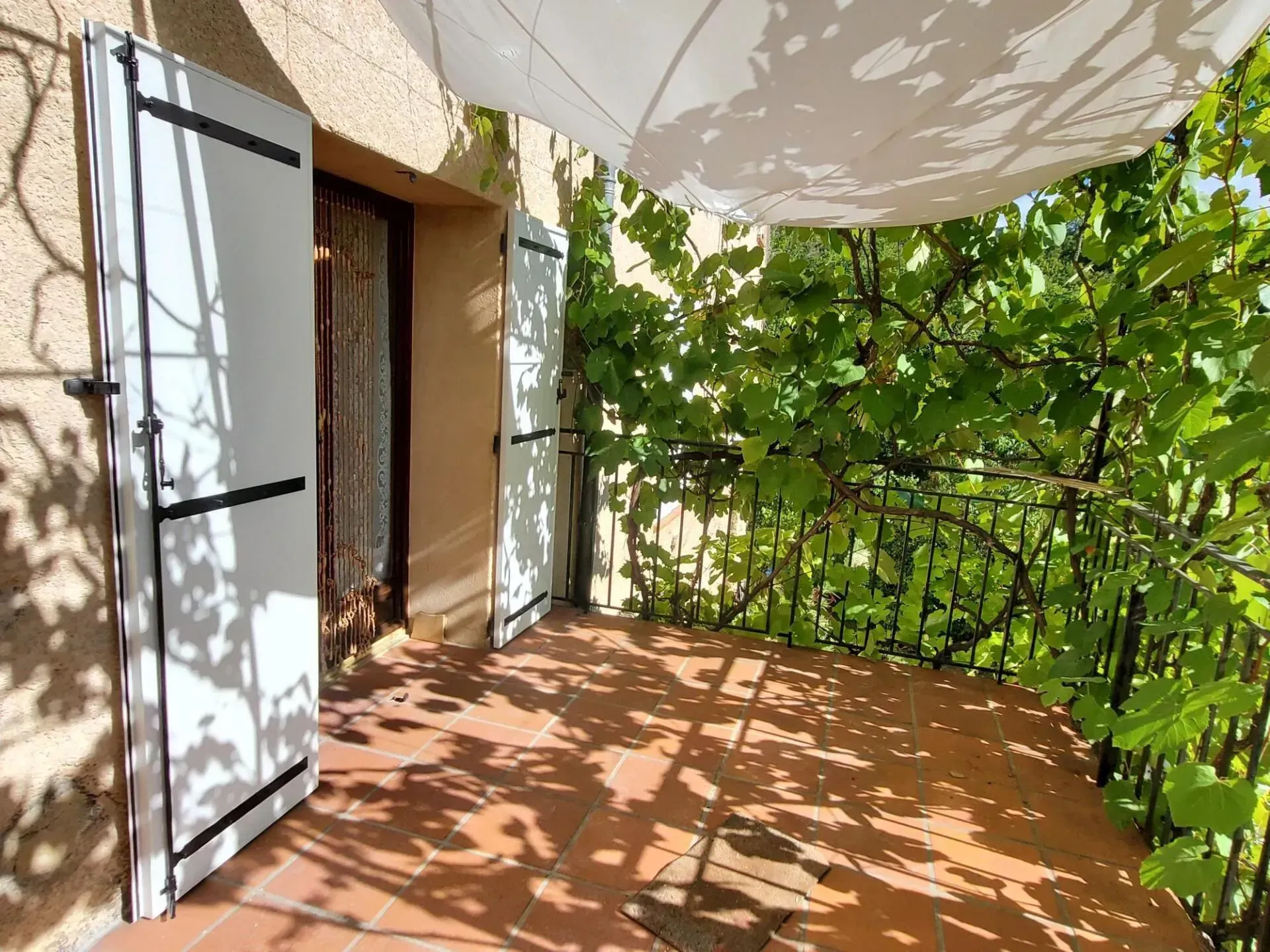 Balcon aux volets blancs ouverts, donnant sur une végétation luxuriante.