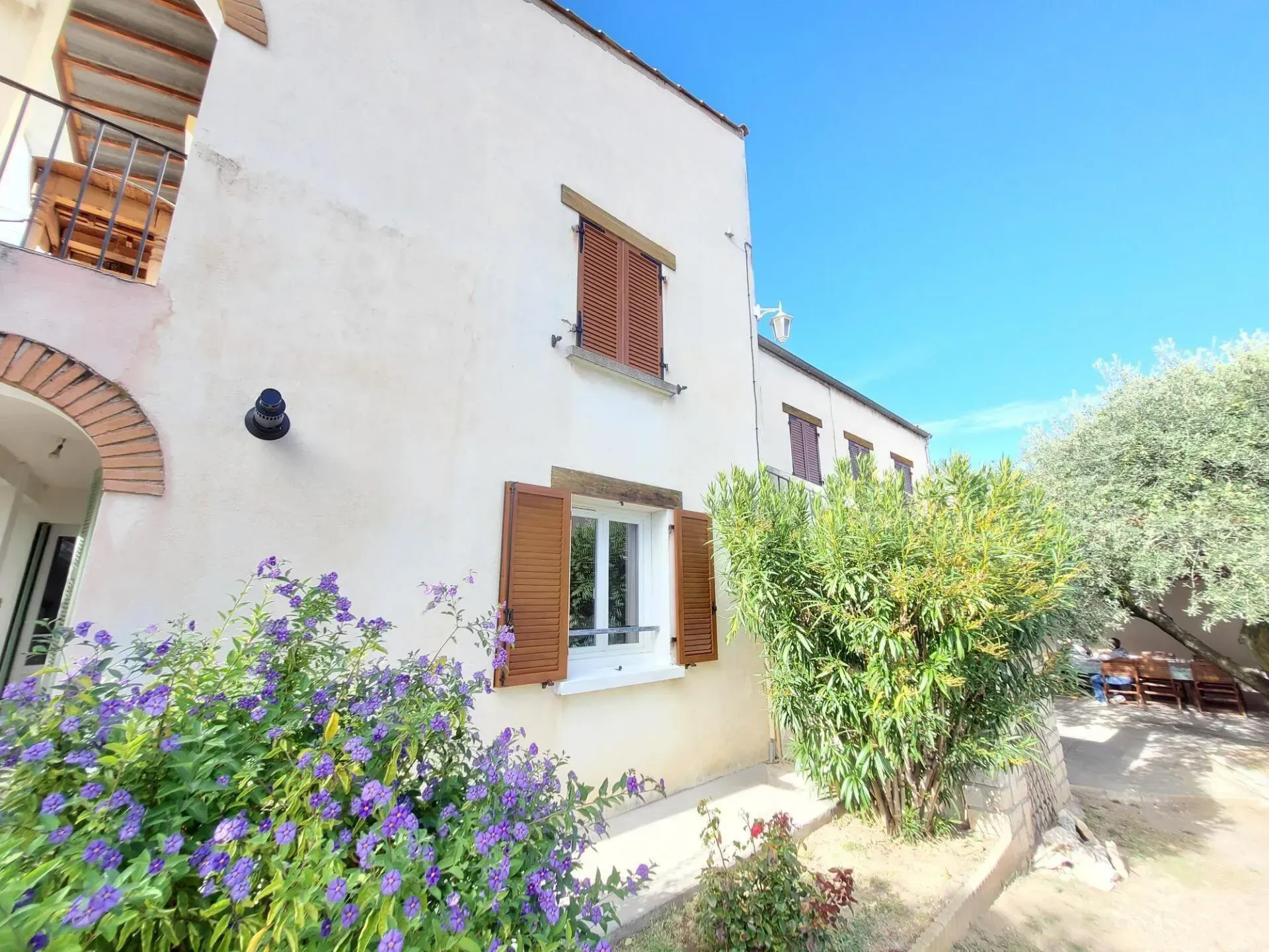 Bâtiment blanc aux volets marron et balcon sous un ciel d'un bleu éclatant.