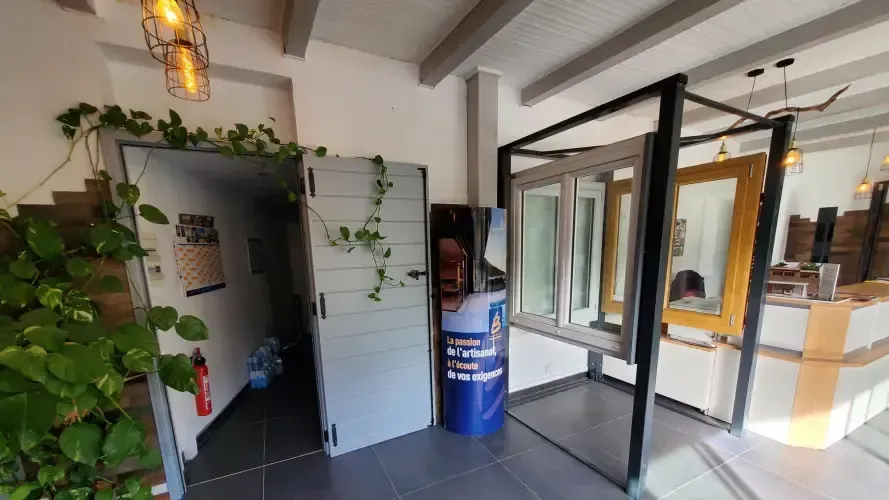 Intérieur d'un bâtiment avec un sol carrelé gris, des vitrines et une porte ornée de plantes