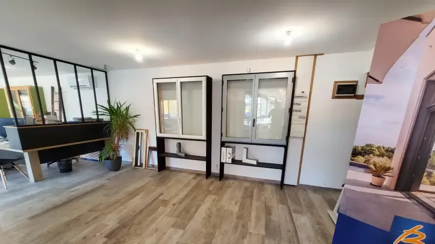 Salle d'exposition avec deux fenêtres, une verrière et un roll-up 