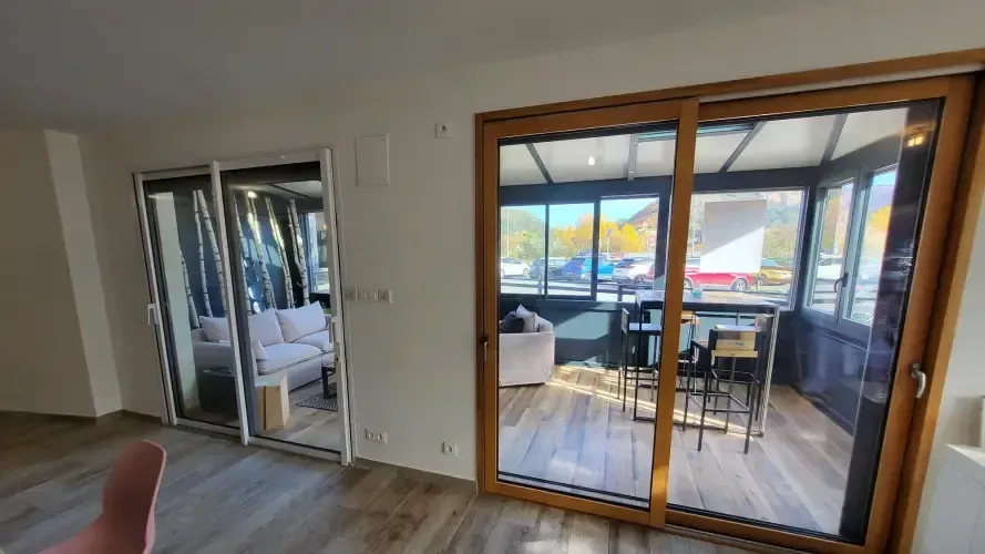 Vue intérieure : portes coulissantes en verre donnant sur une salle à manger. Une autre porte vitrée, à gauche, mène à un coin salon.