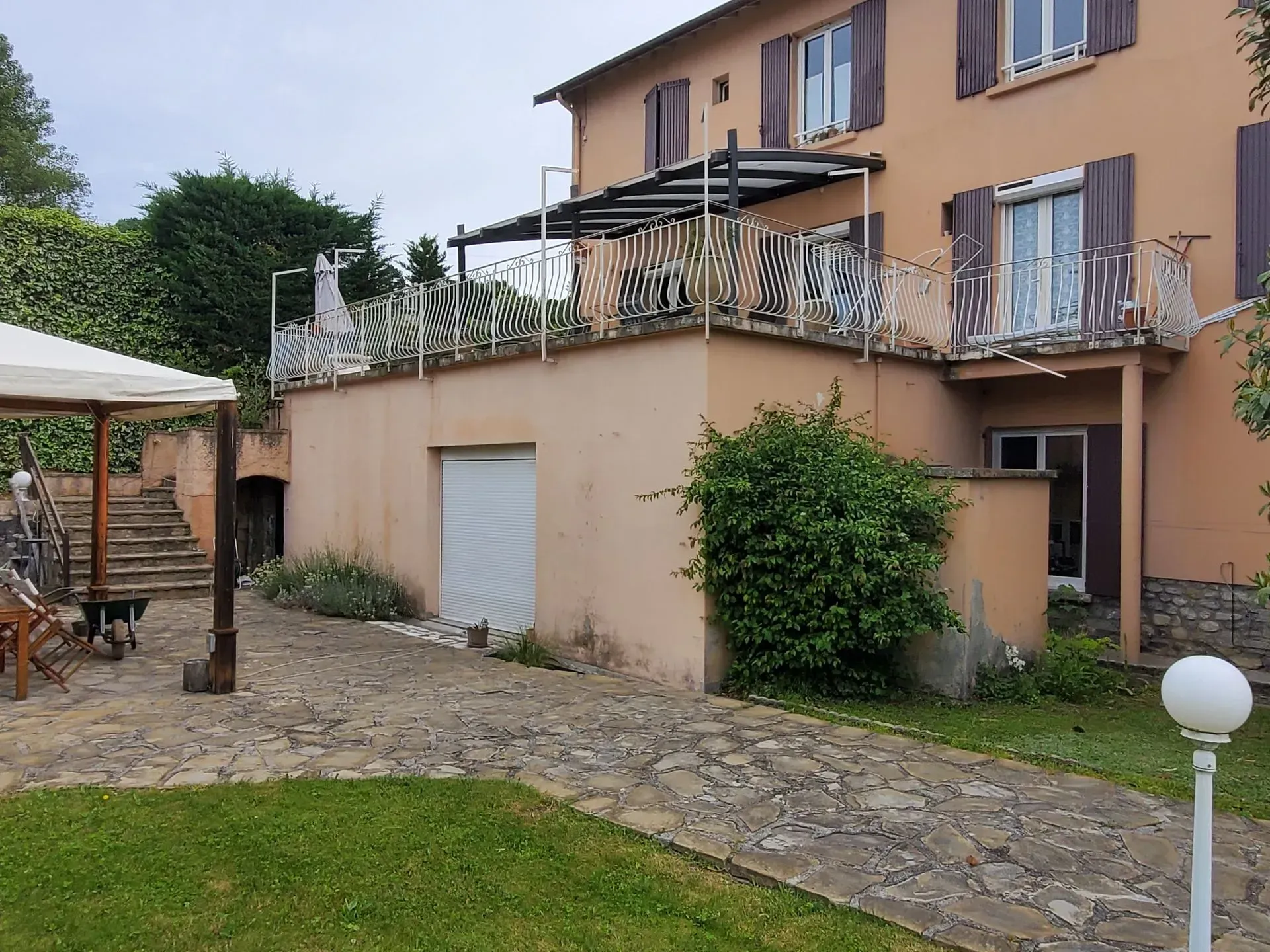 Bâtiment de deux étages couleur pêche avec terrasse et patio en pierre. Une pelouse verte se trouve au premier plan.