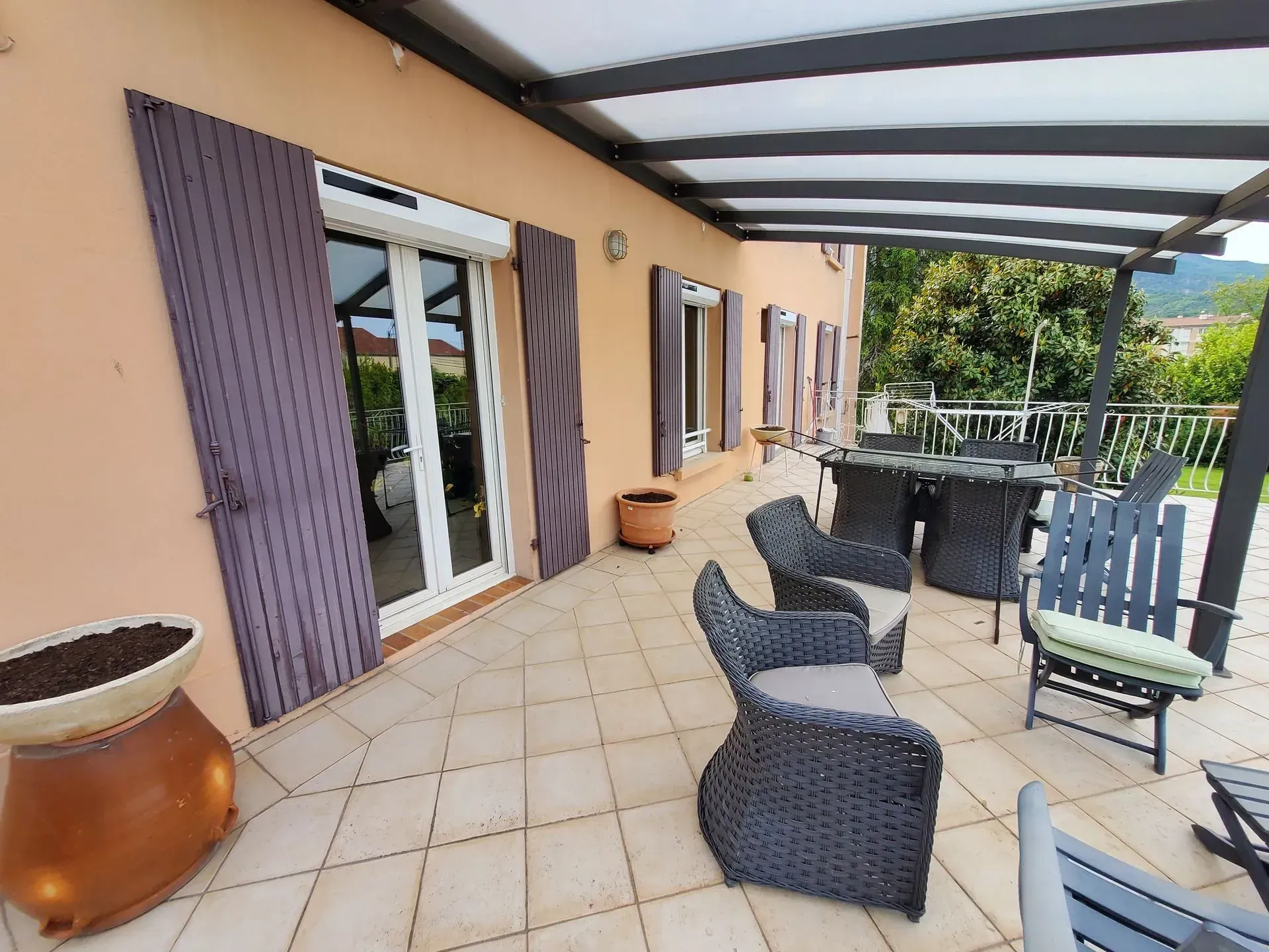 Terrasse avec chaises en osier, table et pergola ombragée. Murs orange et vue sur les arbres.