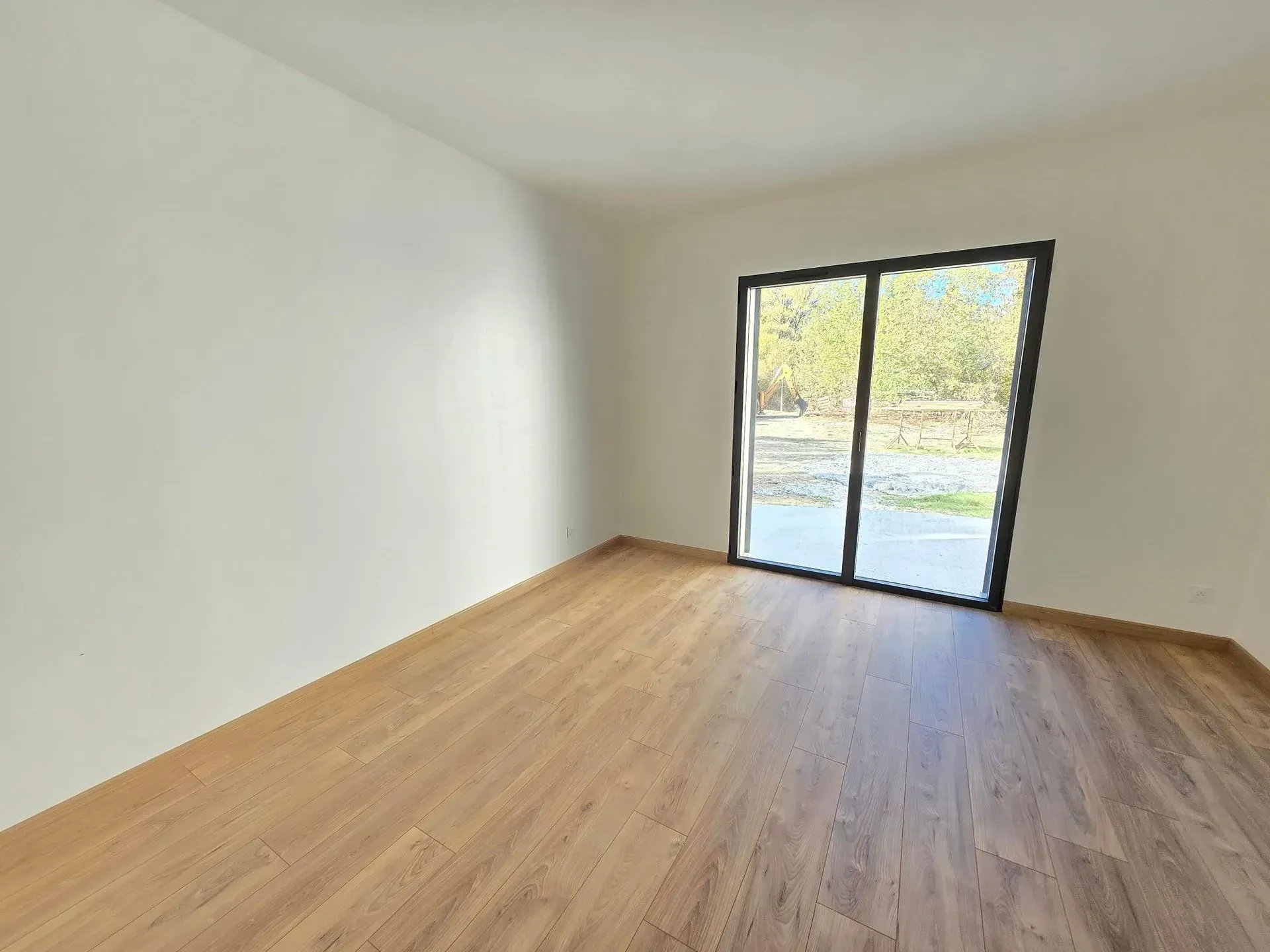 Pièce vide avec parquet, murs blancs et grande porte coulissante en verre.