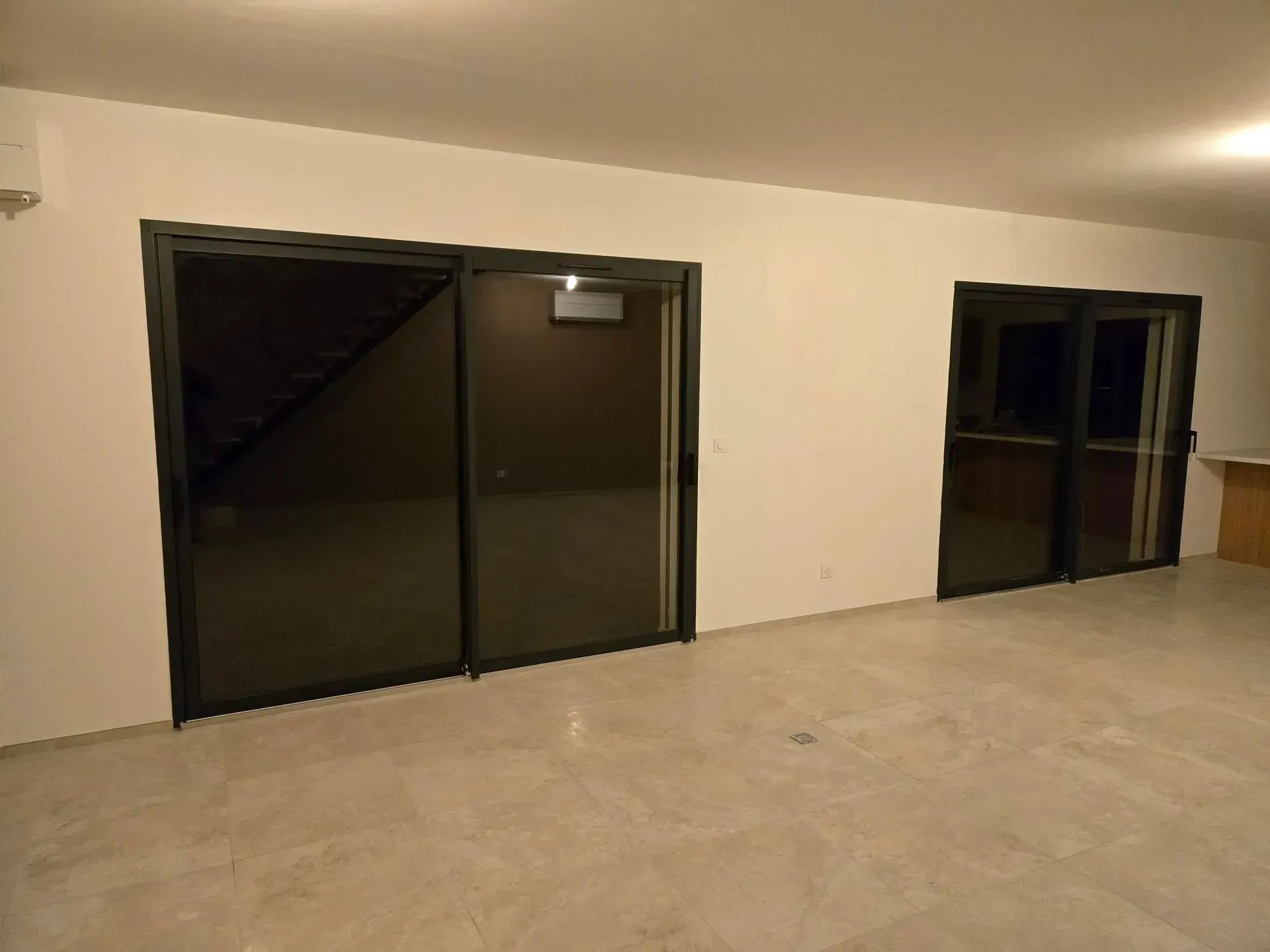 Deux portes coulissantes en verre à cadre foncé sur un mur blanc. Le sol est en béton.