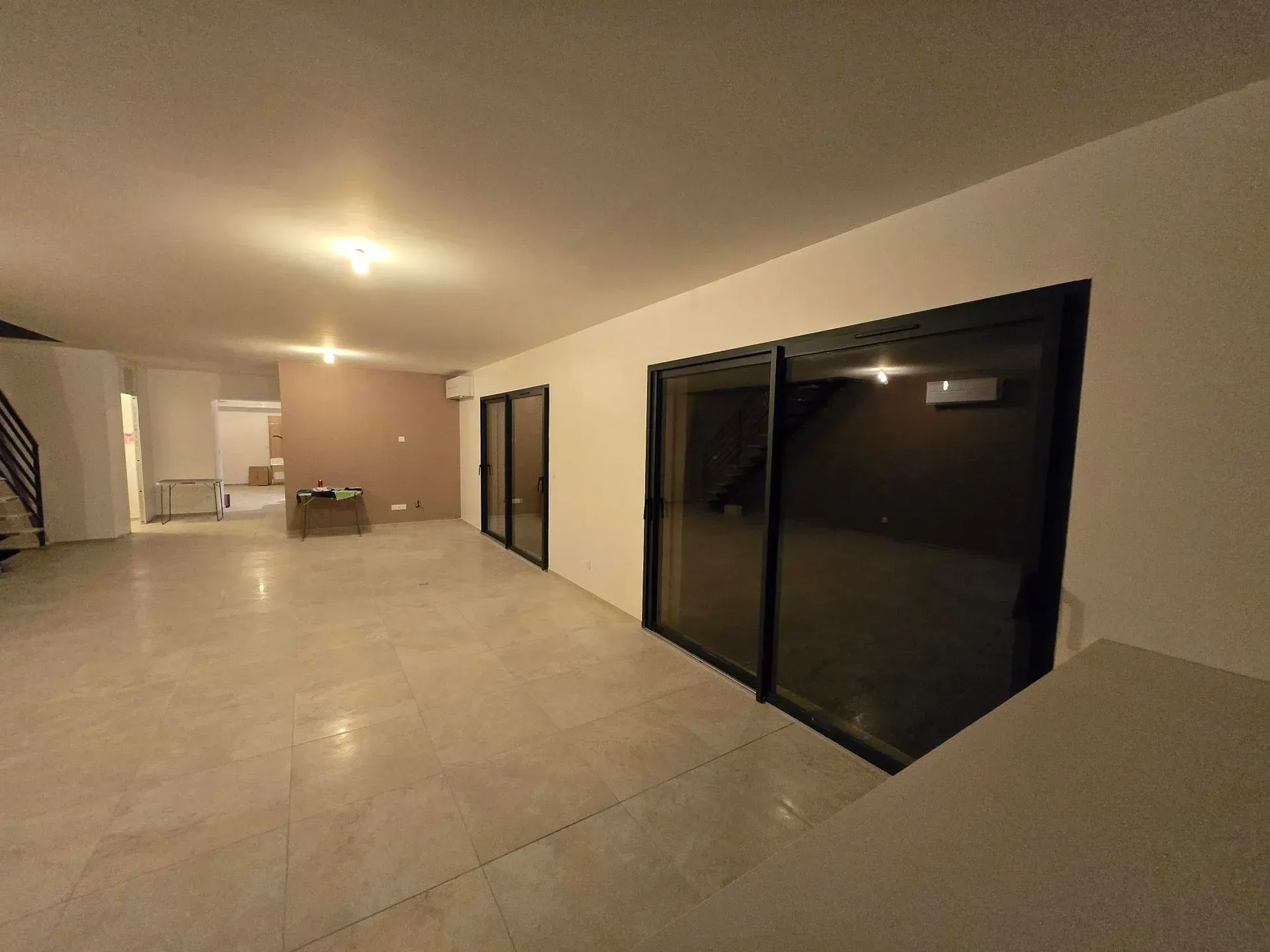 Pièce vide et spacieuse avec de grandes portes coulissantes à cadre noir et un sol carrelé, pouvant correspondre à une maison neuve ou à une rénovation.