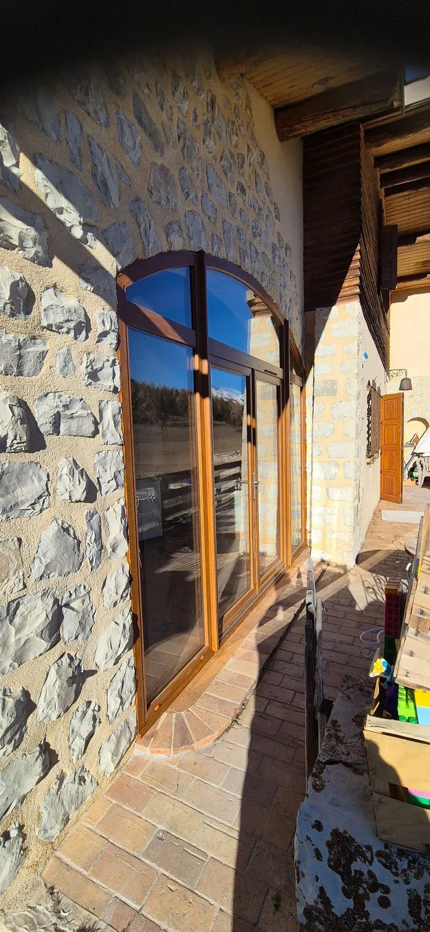Vue extérieure d'un bâtiment en pierre avec des fenêtres cintrées, des boiseries et une terrasse en bois.