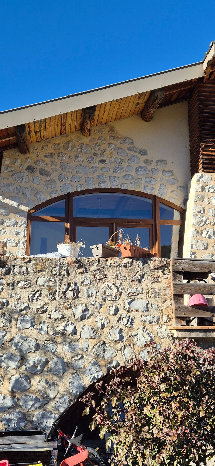 Maison en pierre avec une grande fenêtre cintrée et des boiseries. Ciel bleu visible.