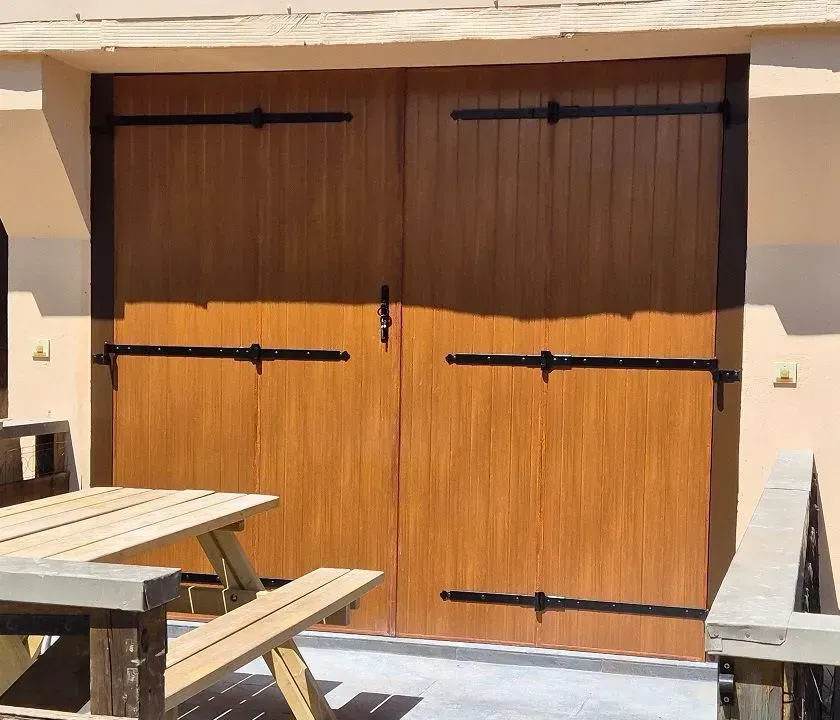 Double porte en bois avec quincaillerie noire, une table de pique-nique devant.