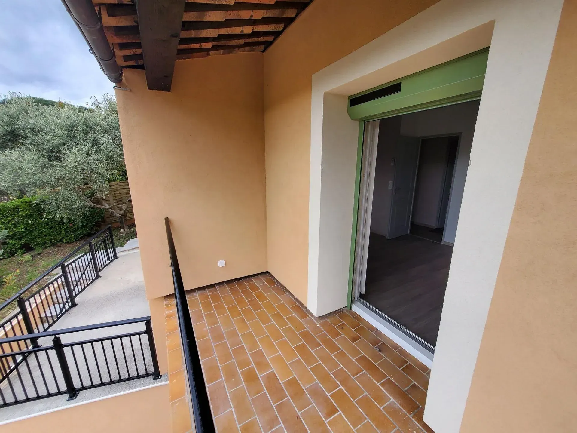 Balcon avec sol en carrelage de terre cuite, rambarde noire et porte ouverte sur un espace intérieur.