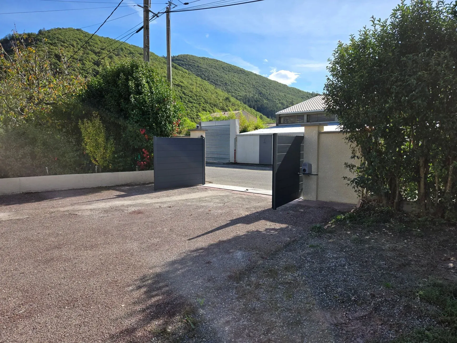 Allée carrossable ouverte donnant sur une allée de gravier menant à une maison. Collines verdoyantes en arrière-plan.