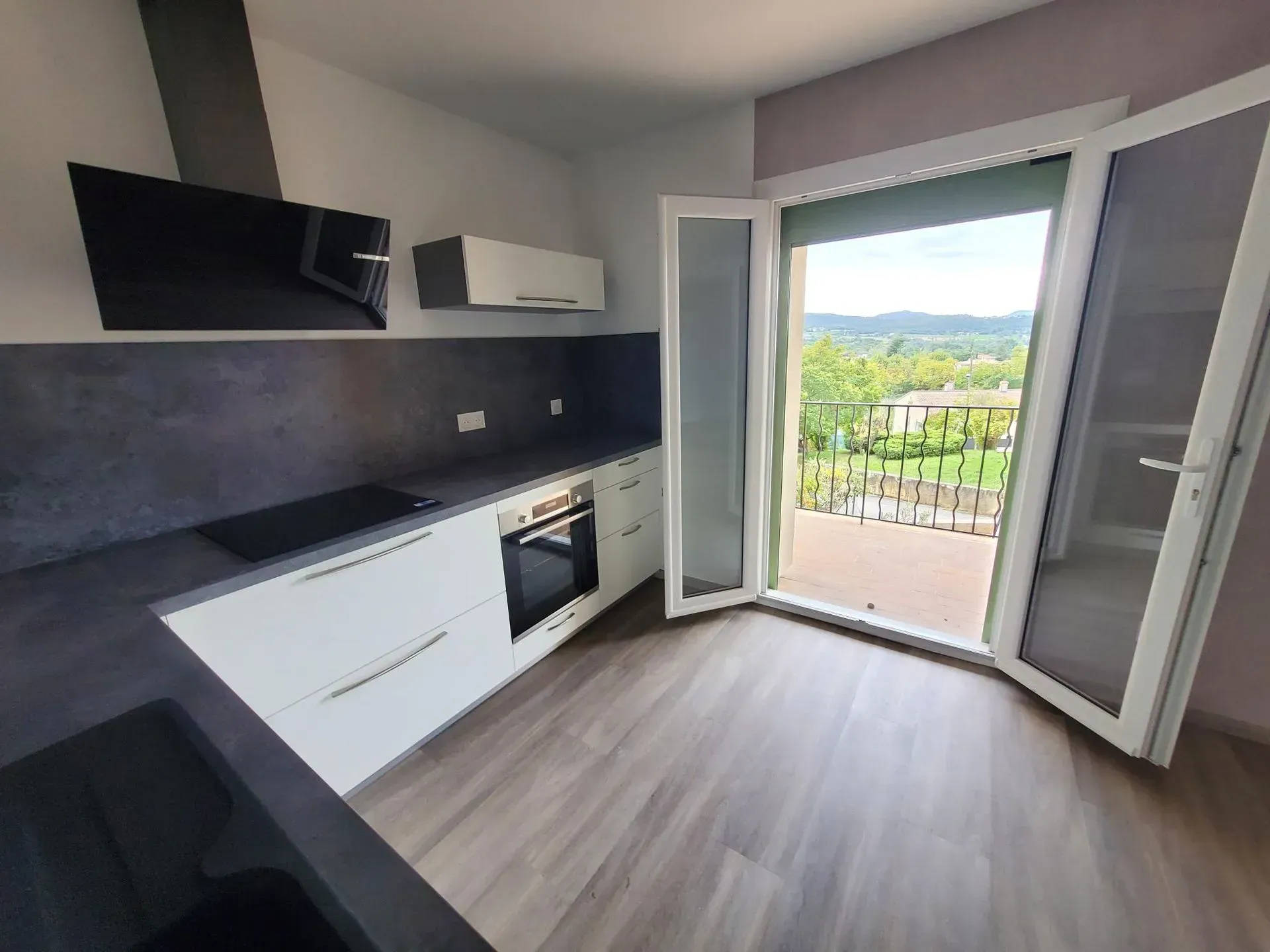 Cuisine moderne avec placards blancs, plans de travail foncés et accès au balcon.