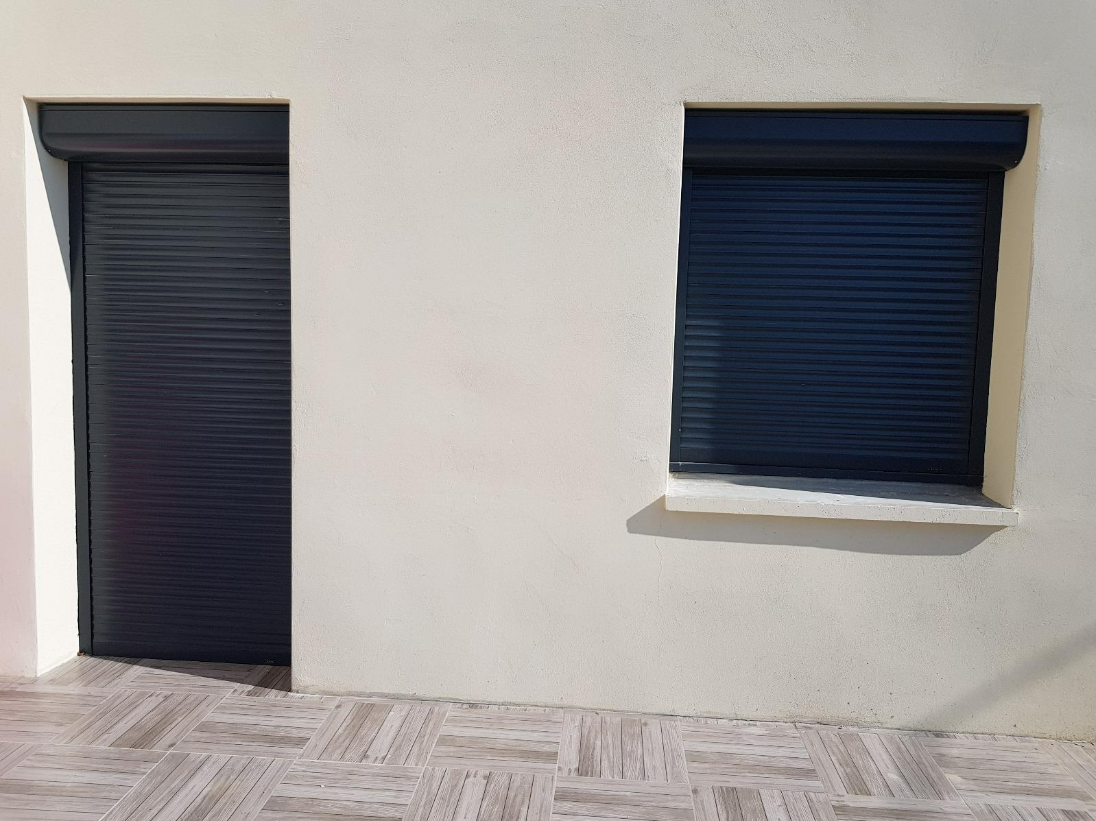 Maison neuve avec volets roulants noirs sur une porte et une fenêtre en façade