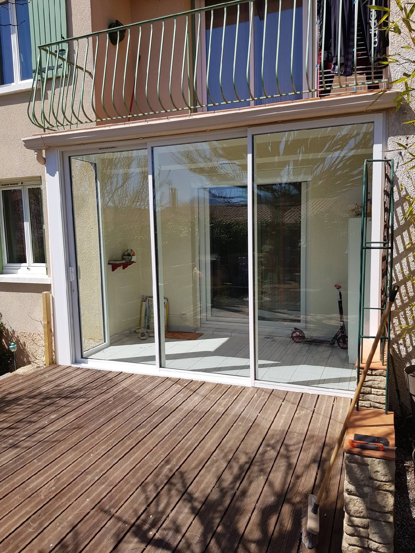 Véranda avec portes coulissantes en verre, construite sur une terrasse en bois, balcon au-dessus