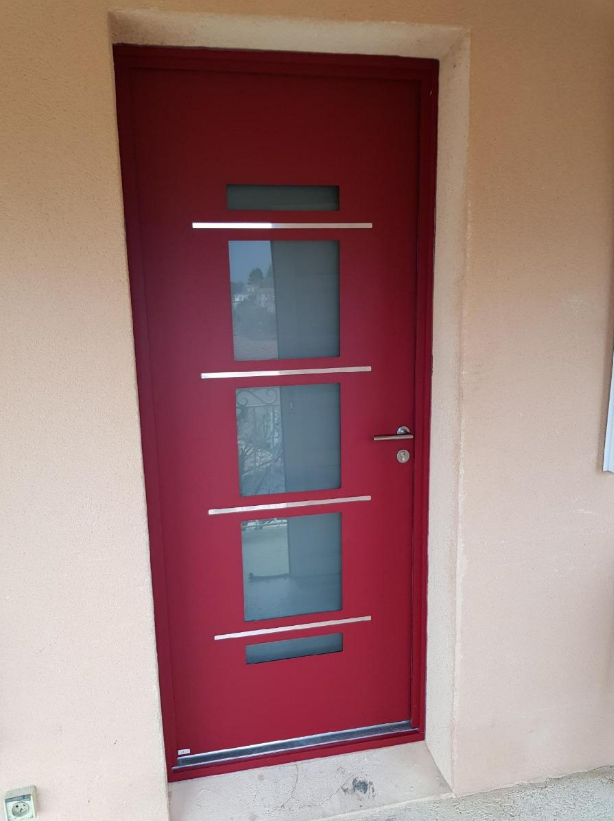 Porte d'entrée rouge avec trois carreaux de verre carrés et des accents horizontaux argentés.