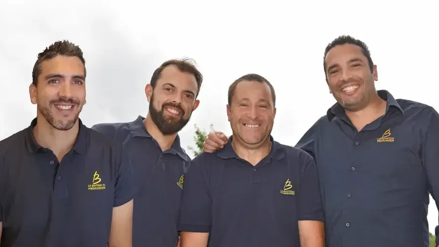 Quatre hommes en chemises bleues assorties sourient à l'extérieur.