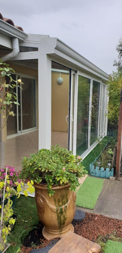 Vue extérieure d'une véranda avec de grandes portes vitrées, des plantes en pot et des zones de gazon