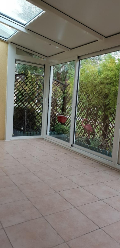 Véranda avec sol carrelé, fenêtres donnant sur la végétation et puits de lumière
