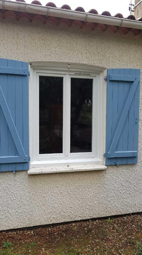 Fenêtre à cadre blanc et volets bleus, sur un mur en stuc.