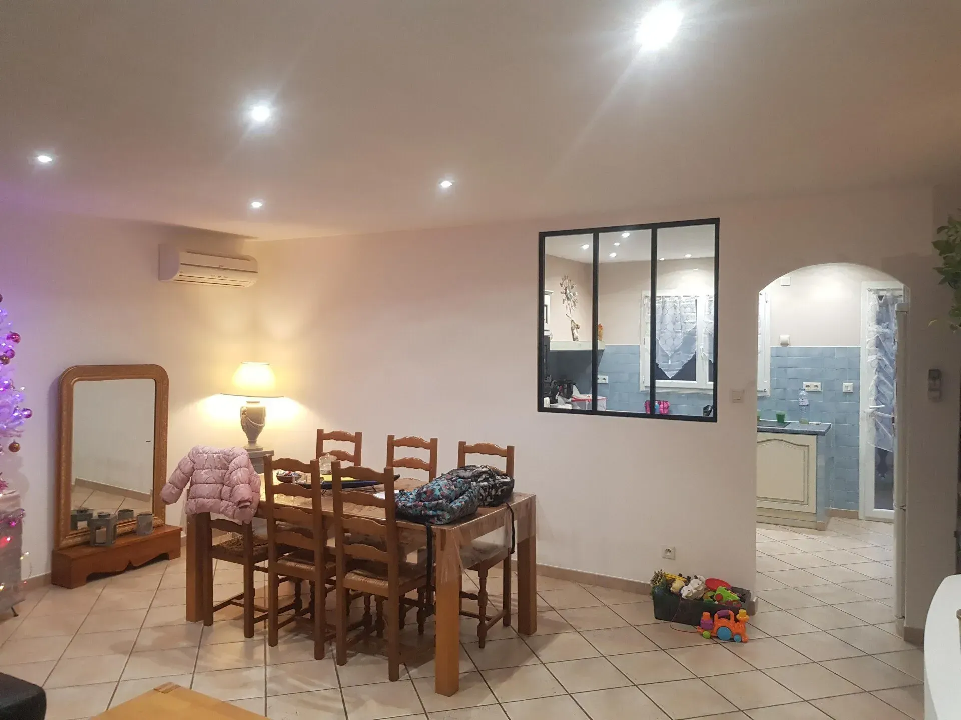 Salle à manger avec une table et des chaises, un miroir et une porte ouverte sur la cuisine.
