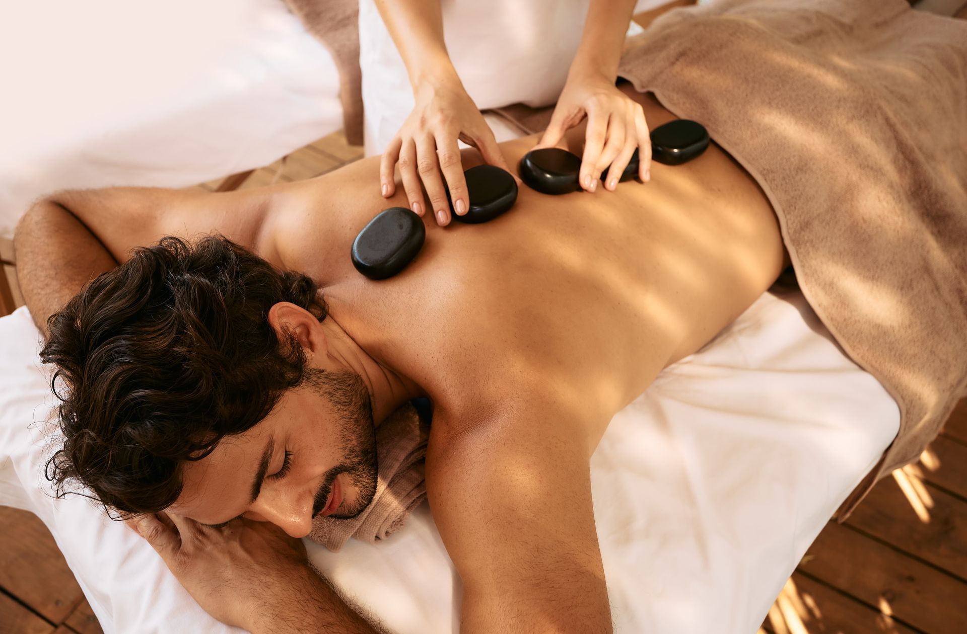 Eine Person genießt eine Hot-Stone-Massage, während sie in einer hellen, ruhigen Umgebung auf einer Liege liegt.