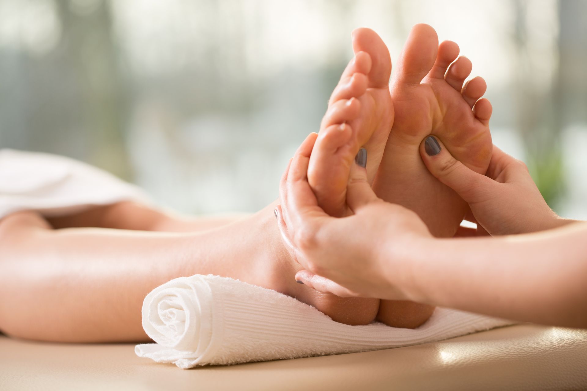 Eine Massagetherapeutin führt eine Fussreflexzonenmassage bei einem Klienten durch, der auf einer Liege mit einem weissen Handtuch ruht.