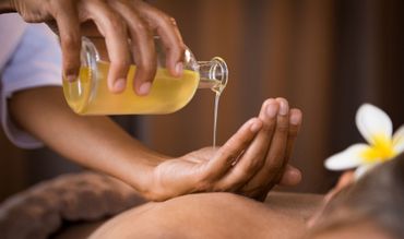 Eine Person genießt eine Hot-Stone-Massage, während sie in einer hellen, ruhigen Umgebung auf einer Liege liegt.