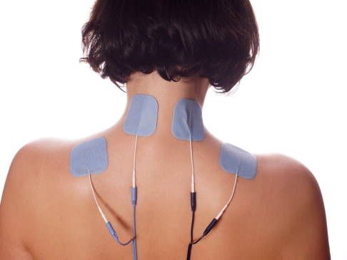Eine Therapeutin führt eine Muschelmassage am oberen Rücken einer Person durch, wobei sie zwei glatte, gerippte Muscheln verwendet.