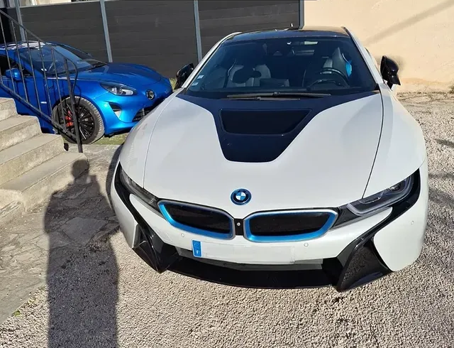 Une BMW i8 blanche avec des touches de bleu est garée à l'extérieur à côté d'une voiture de sport bleue.