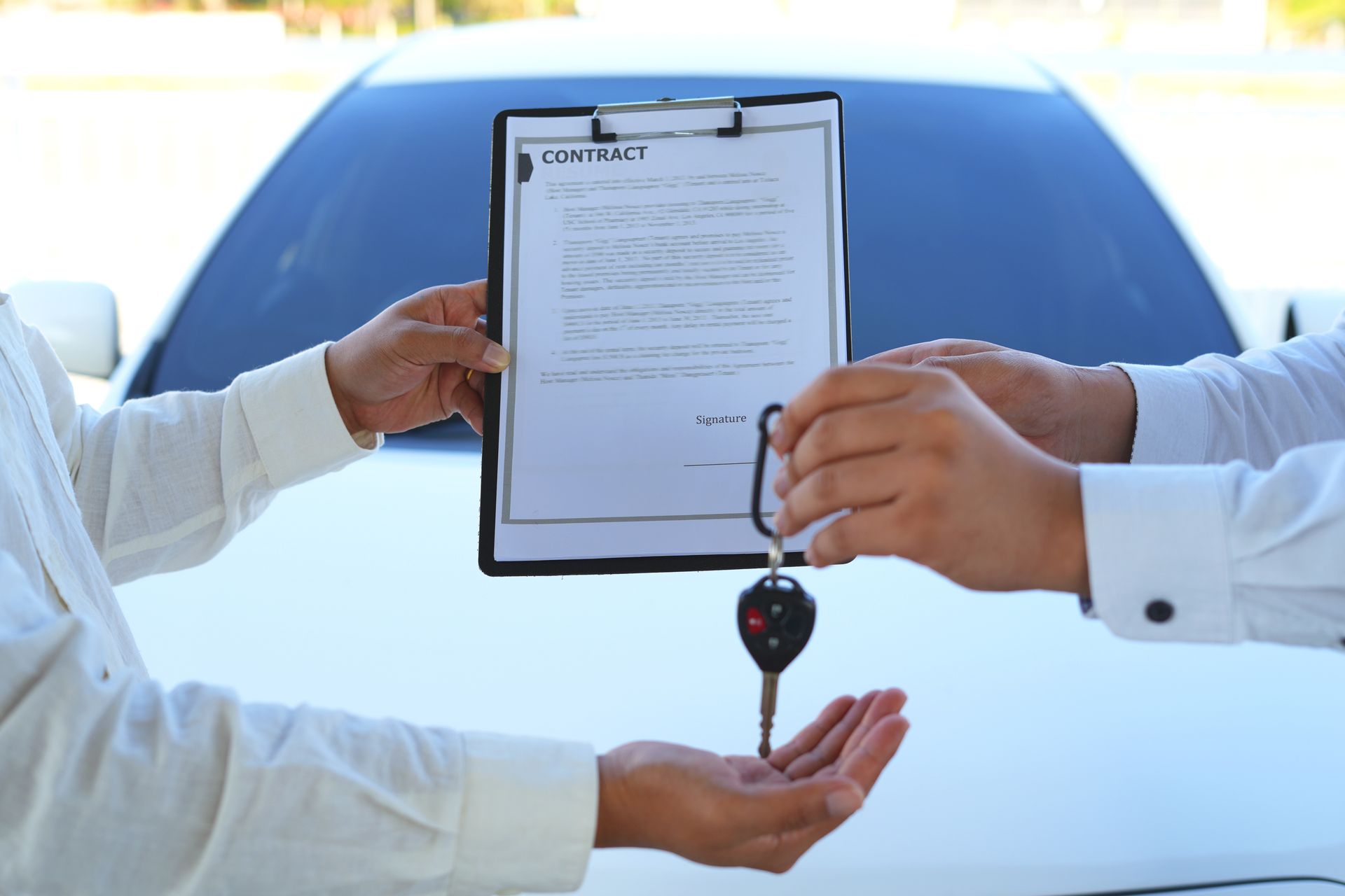Des mains échangent des clés de voiture et un bloc-notes devant une voiture blanche pour la location du véhicule.