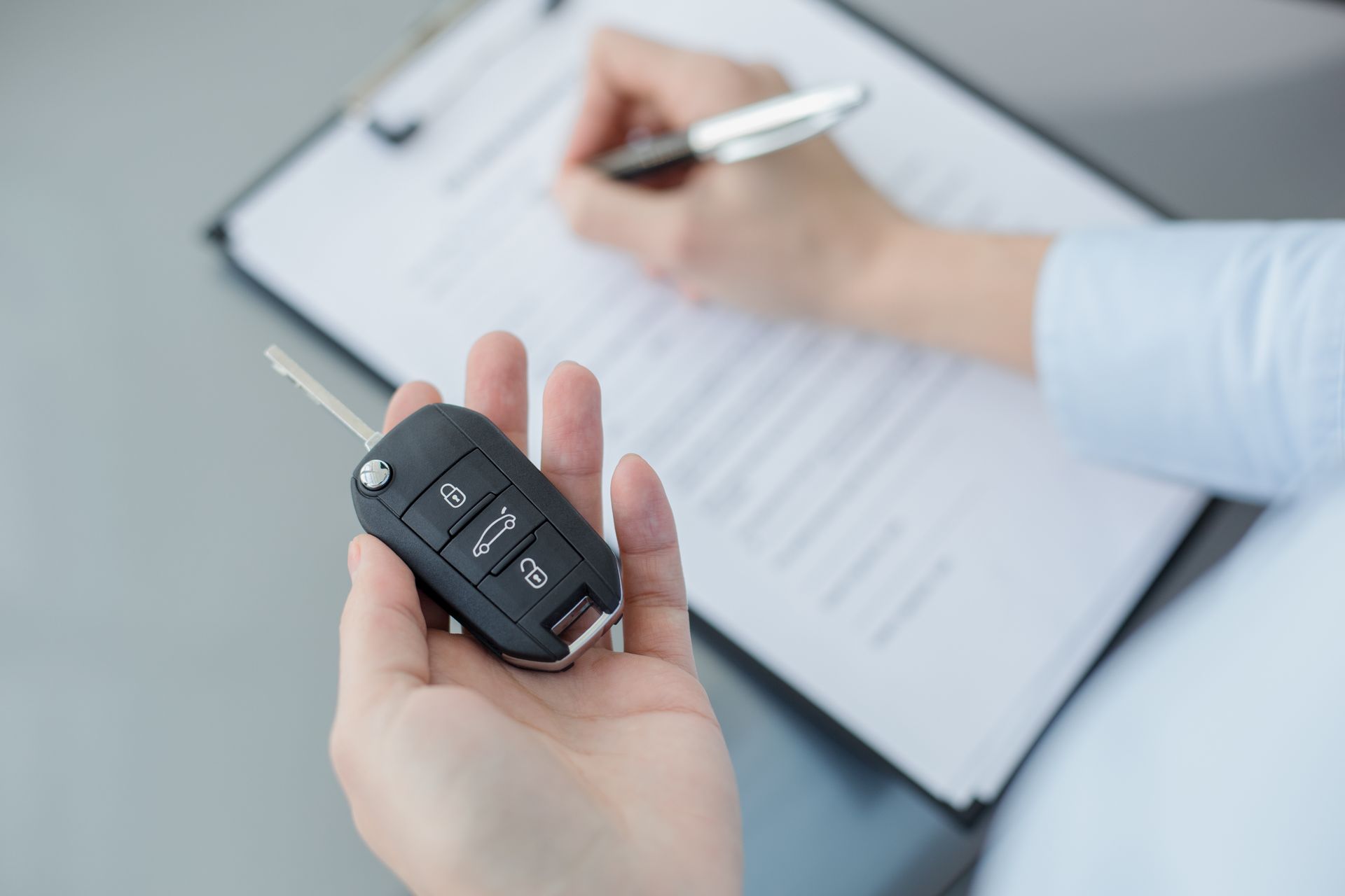 Une personne tient une clé de voiture dans une main et complète un document de l'autre main.