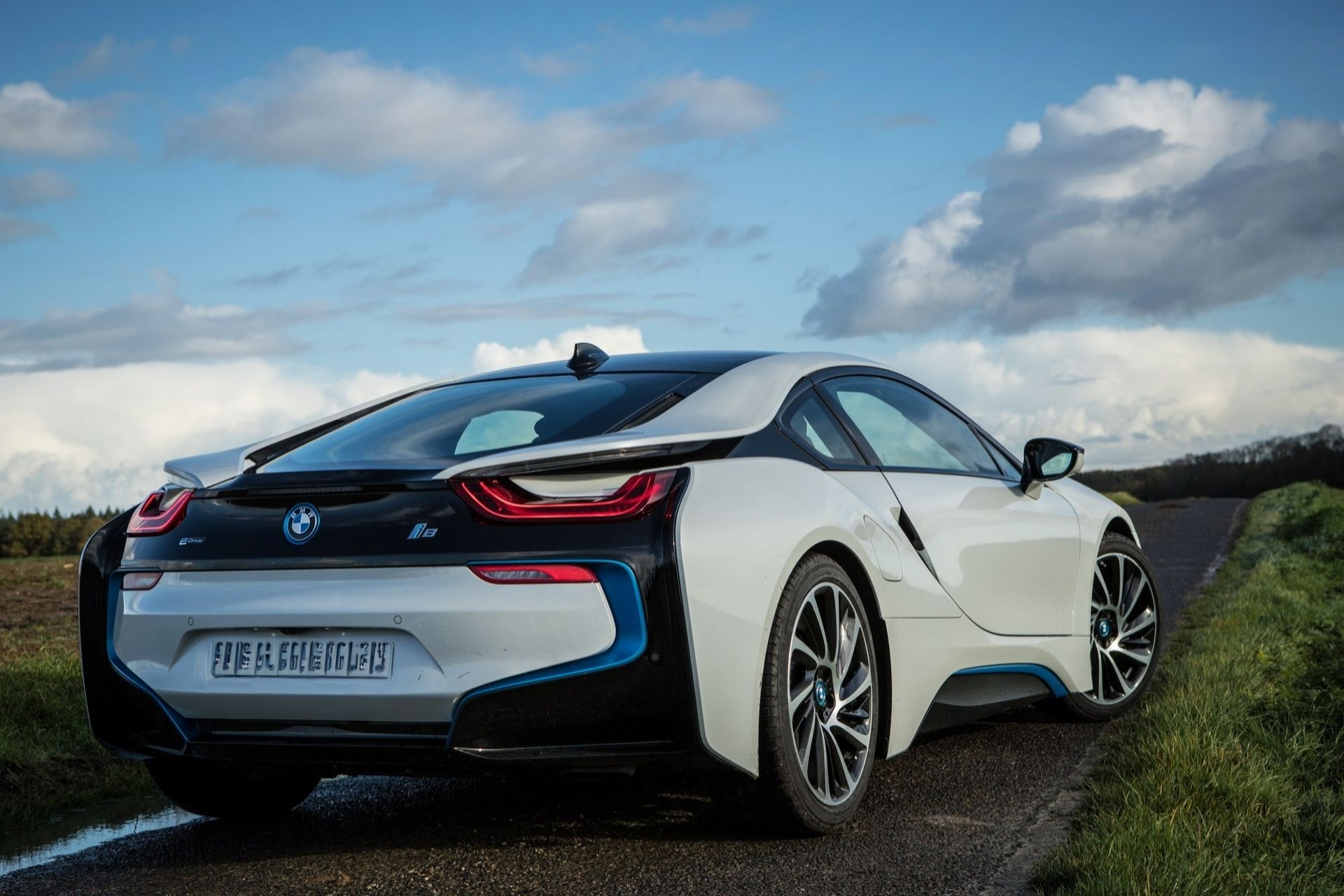 BMW i8 blanche garée sur une colline sous un ciel bleu nuageux