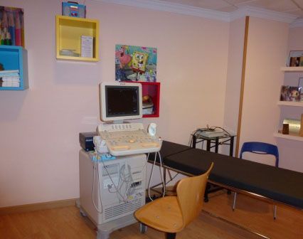 Máquina de ultrasonido en una sala médica con paredes de color rosa, estantes de pared coloridos y arte de Bob Esponja.