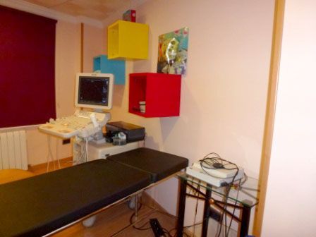 Sala de exámenes médicos: máquina de ultrasonido, mesa de examen, estantes de pared coloridos, persiana de ventana color burdeos.