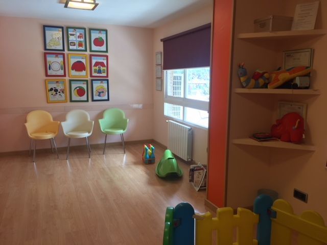 Sala de espera con sillas, obras de arte coloridas, juguetes y estantes.