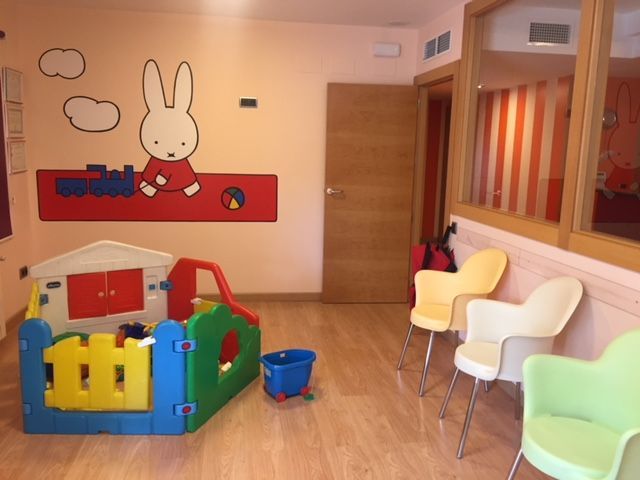 Sala de juegos con casa de juguetes, mural de conejito, sillas y puerta.