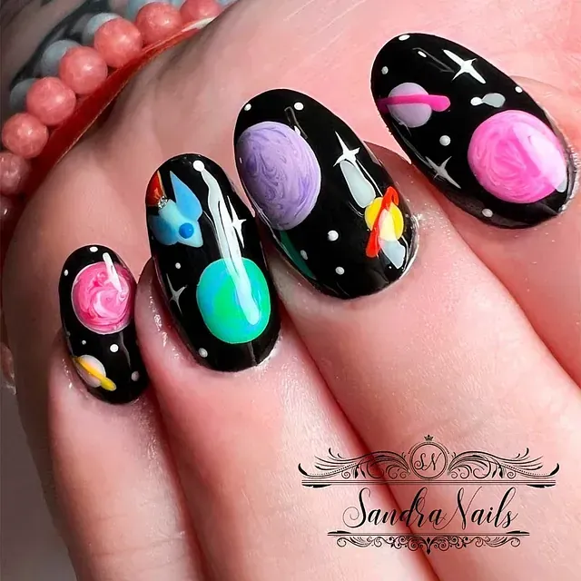 Un primer plano de las uñas de una persona con planetas pintados en ellas.