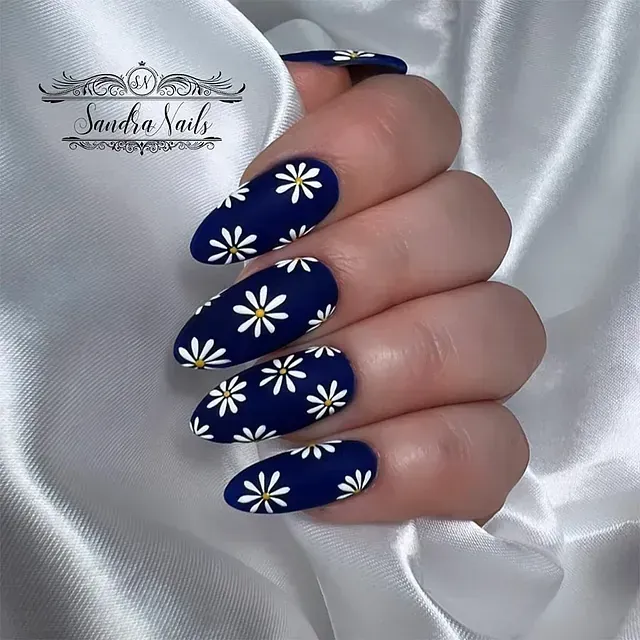 Las uñas de una mujer están pintadas de azul con margaritas blancas.