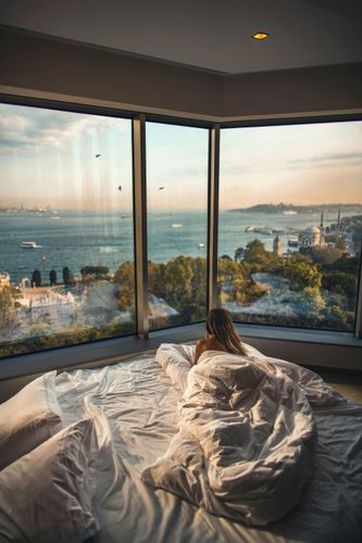 A woman is laying on a bed with a view of the ocean.