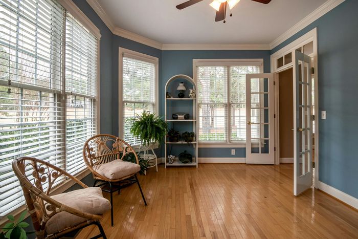 A living room with hardwood floors , blue walls , a ceiling fan and a wicker chair.